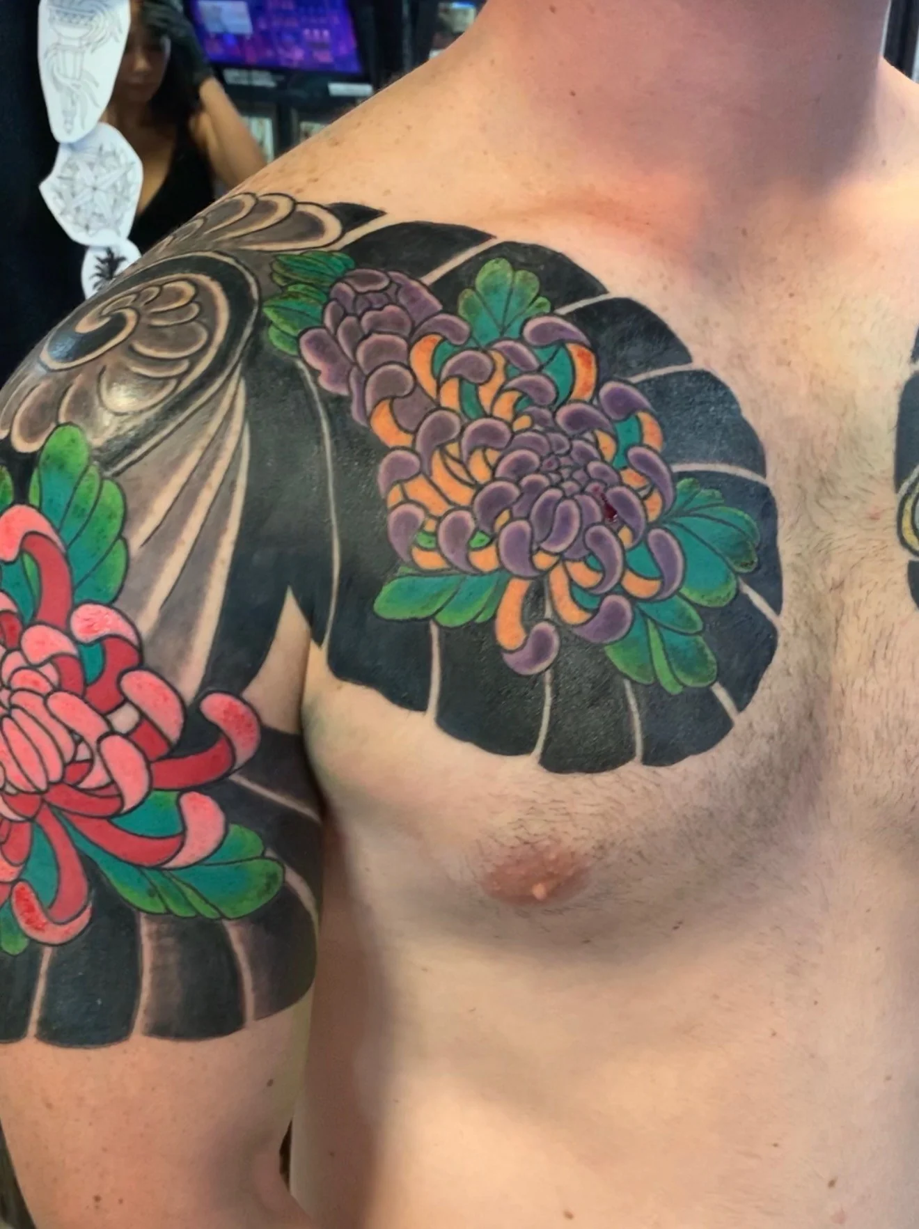 Japanese Wabori chest tattoo with a red chrysanthemum on one panel and a purple-and-orange chrysanthemum on the other, against deep black with green leaves, by Tim Goodrich at his Waikiki tattoo shop, Hawaii.
