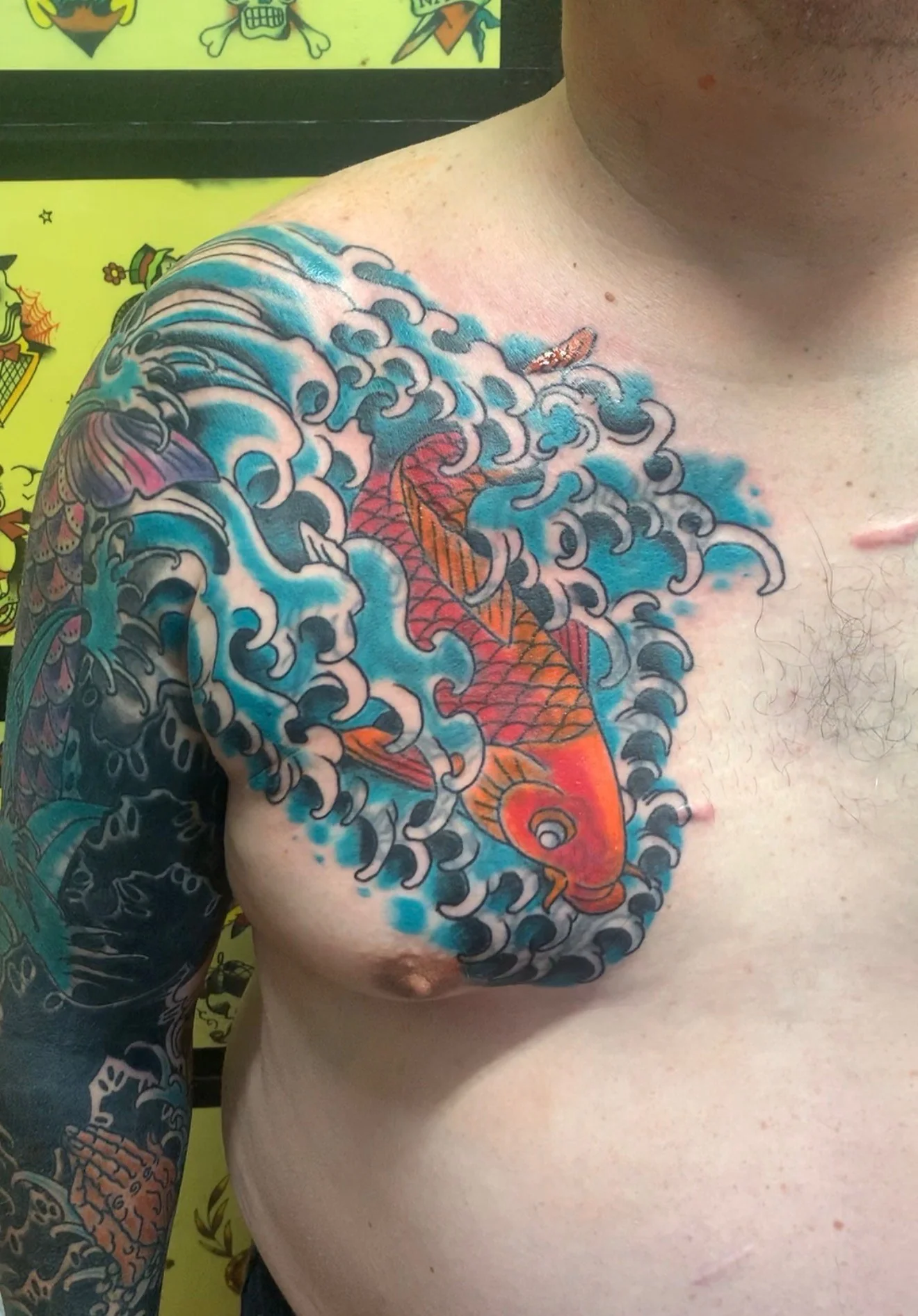 Japanese Wabori color tattoo of a saturated orange koi swimming through cresting blue waves on the chest, by Tim Goodrich at his Waikiki tattoo shop, Hawaii.