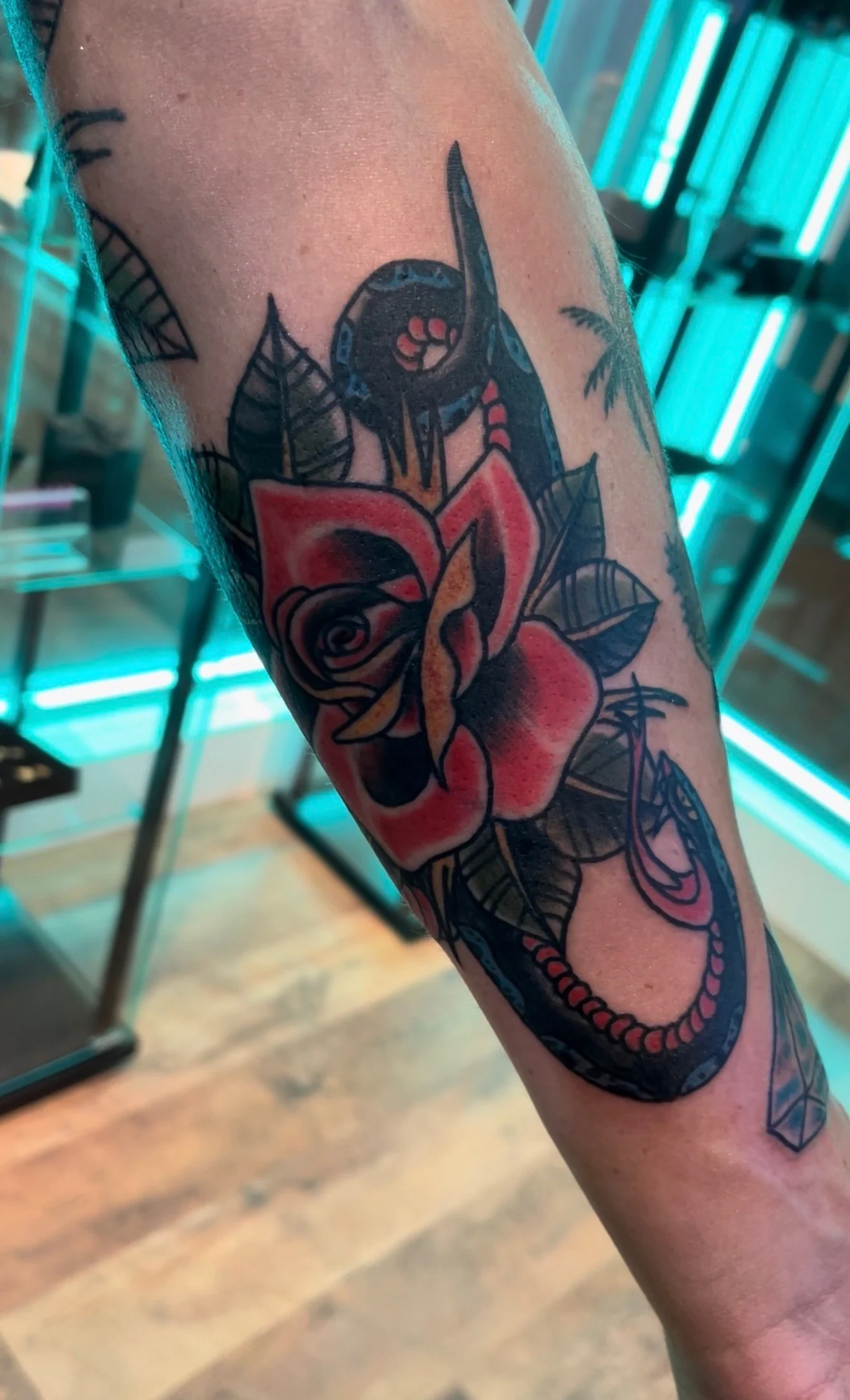 American Traditional color tattoo of an open red rose with a red-and-black snake and a black anchor on the forearm, by Tim Goodrich at his Waikiki tattoo shop, Hawaii.